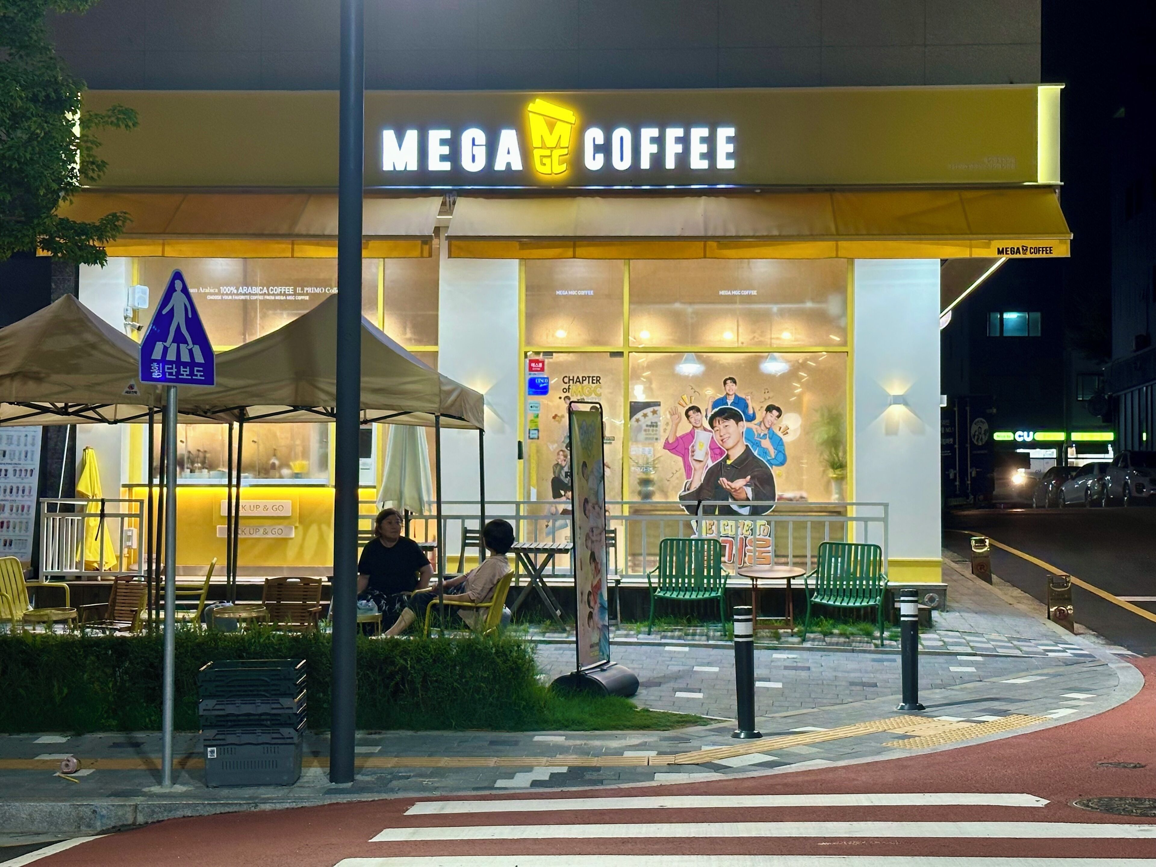 Un café appelé « MEGA COFFEE » avec une terrasse et un panneau indiquant un passage piéton.