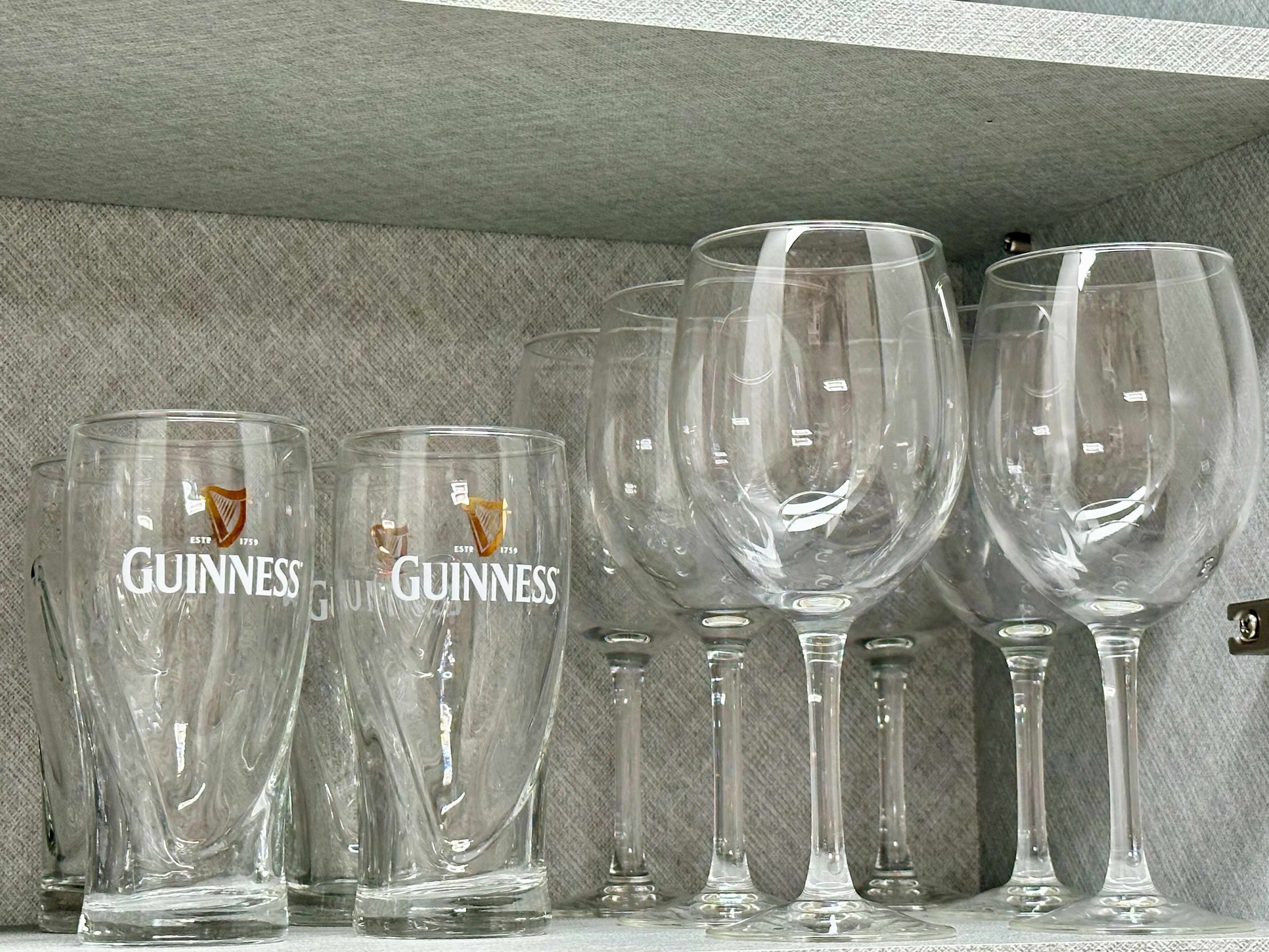 A collection of clear glassware with the Guinness logo, arranged on a shelf.