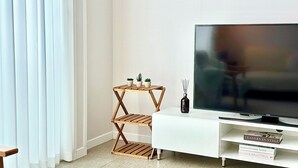 A living room with a white TV stand, a wooden shelf with plants, and a book titled 'Leaders in Style'.