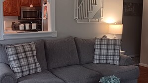 A living room with a gray sofa, a white coffee table, a ceiling fan, and a kitchen area in the background. - Serene 2-bedroom bed & breakfast in charming Saugerties (Saugerties)