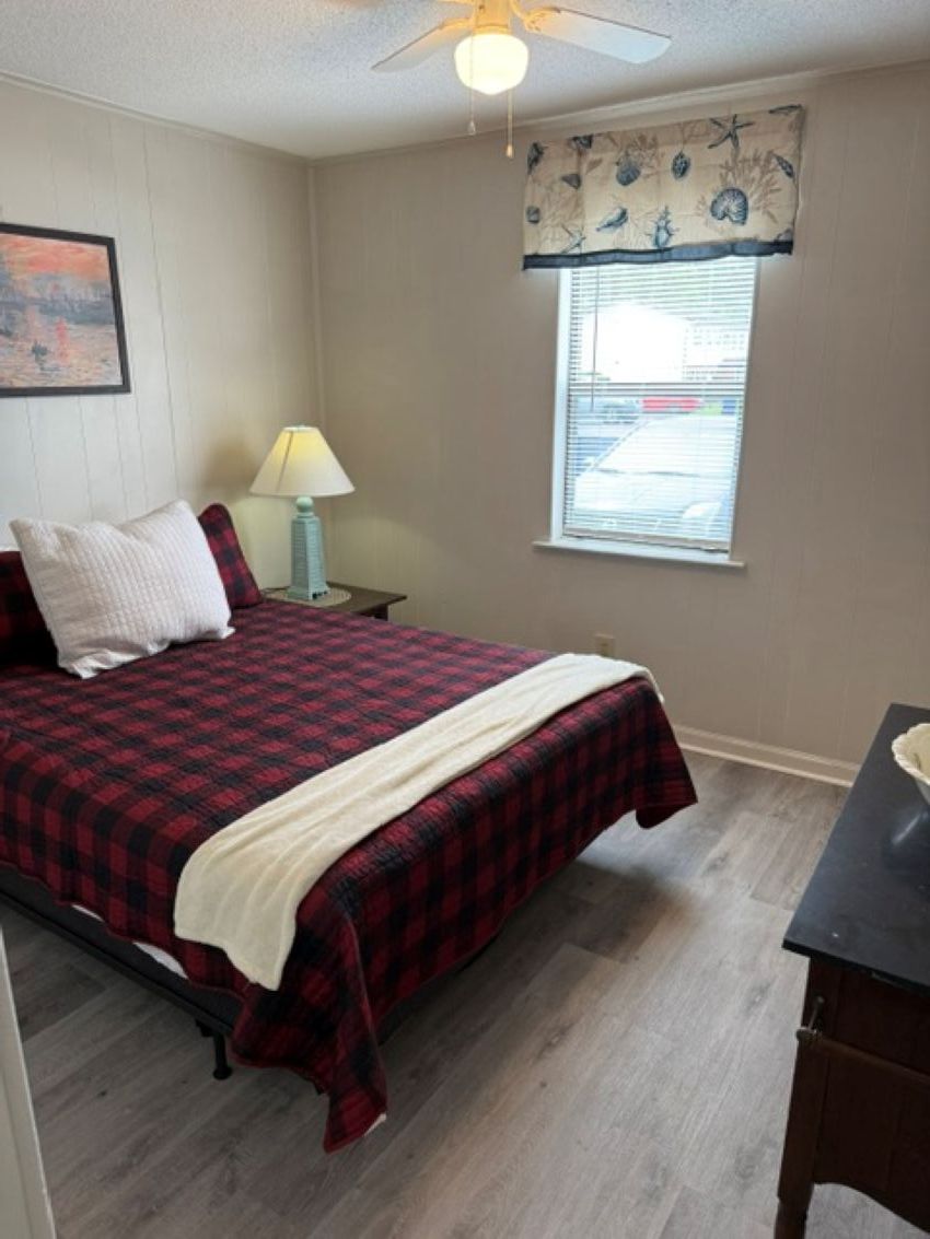 A bedroom with a bed, a nightstand, a lamp, a window with blinds, and a ceiling fan.