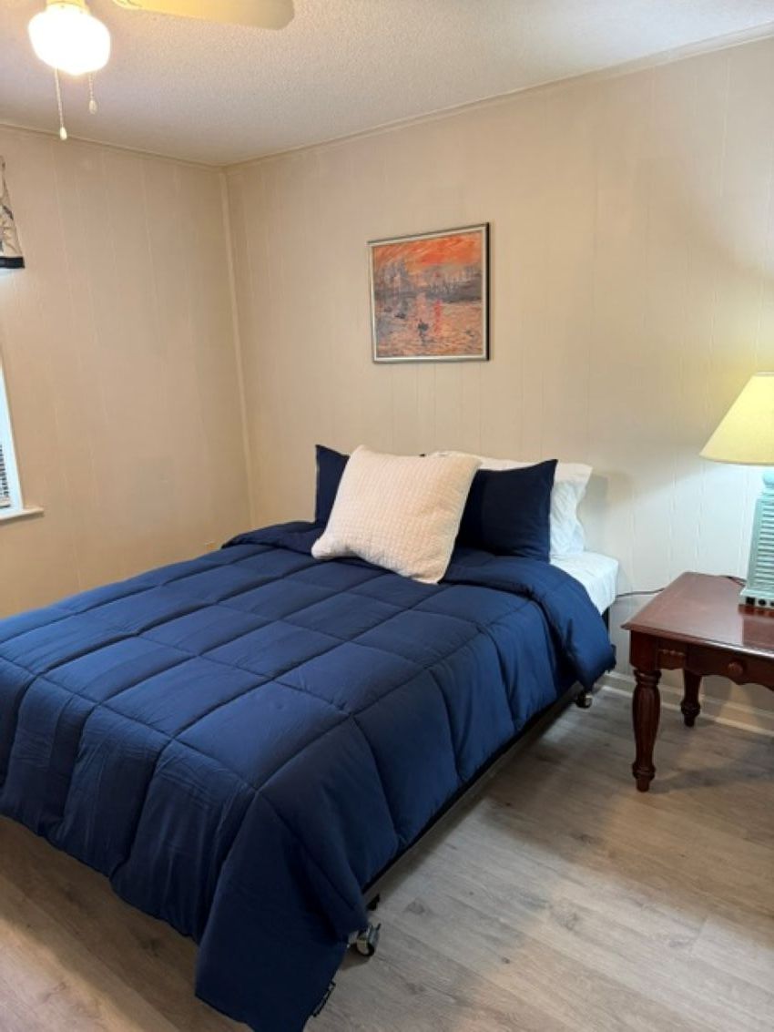 A bedroom with a bed, a nightstand, a lamp, and a painting on the wall.