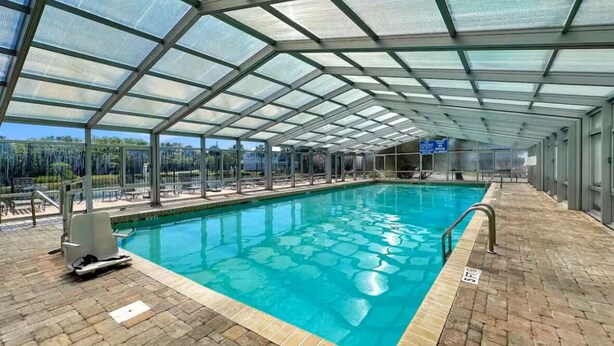 En indendørs swimmingpool med glasloft, klart vand og flisegulv.