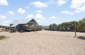 A beachside building with a covered patio, picnic tables, and a volleyball net. - Resort Club Cottage on the lagoon (Edisto Island)