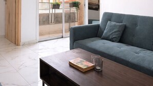 Una sala de estar moderna con un sofá gris, una mesa de centro de madera y un ventanal con vistas a edificios.