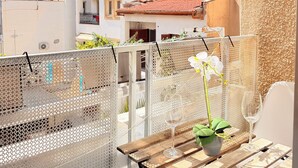 Un balcón con una mesa de madera, plantas en macetas y vista de edificios cercanos.
