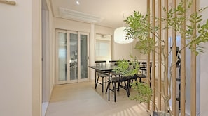 Un comedor con una mesa y sillas, una planta en maceta y un ventanal corredero que da a otra habitación.
