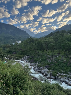 A mountainous landscape with a river, greenery, and a building with a traditional architectural style.