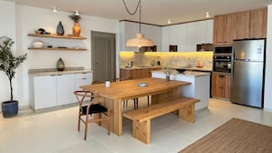 A modern kitchen with wooden cabinets, a stainless steel refrigerator, and a wooden dining table with benches. - Fouka North Coast CL9-CH22-01 (Marsa Matrouh)