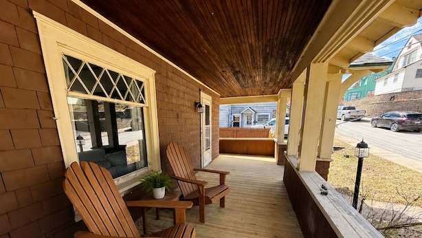 Eine Holzterrasse mit zwei Adirondack-Stühlen, einem kleinen Tisch und einem Blumentopf.