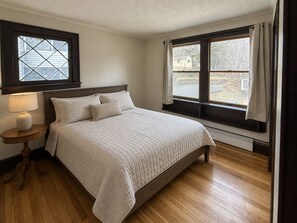 Un dormitorio con cama, mesita de noche, ventana con cortinas y radiador.