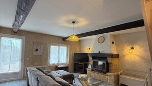 A living room with a sofa, a TV, a fireplace, and a wooden ceiling beam. - Liorelys en Provence - Charming house with swimming pool (L'Isle-sur-la-Sorgue)