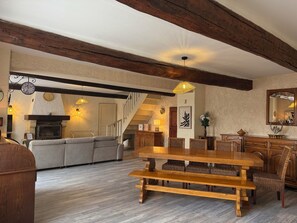 Ein großzügiger Wohnbereich mit Kamin, Sofa, Esstisch und Holzbalken.