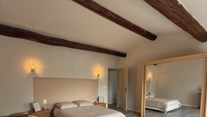 A bedroom with a bed, bedside tables, a dresser, a mirror, and wooden beams on the ceiling. - Liorelys en Provence - Charming house with swimming pool (L'Isle-sur-la-Sorgue)