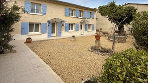 A two-story building with blue shutters, a tiled patio, and a gravel courtyard. - Liorelys en Provence - Charming house with swimming pool (L'Isle-sur-la-Sorgue)