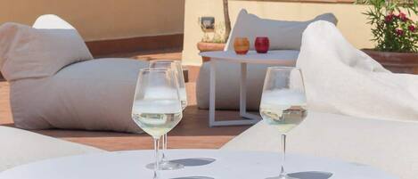 A terrace with a white table, two glasses of white wine, a white sofa, and a potted plant.