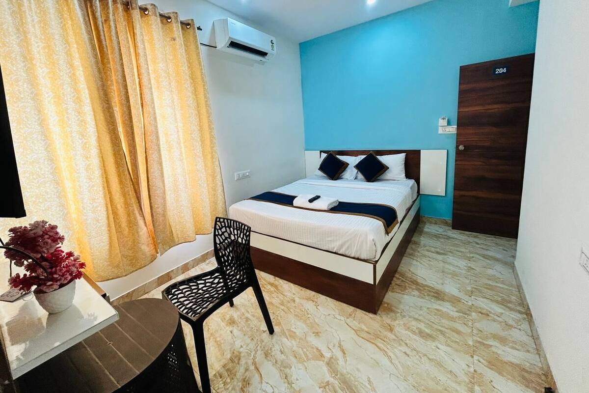 A bedroom with a bed, a desk, a chair, and an air conditioning unit.