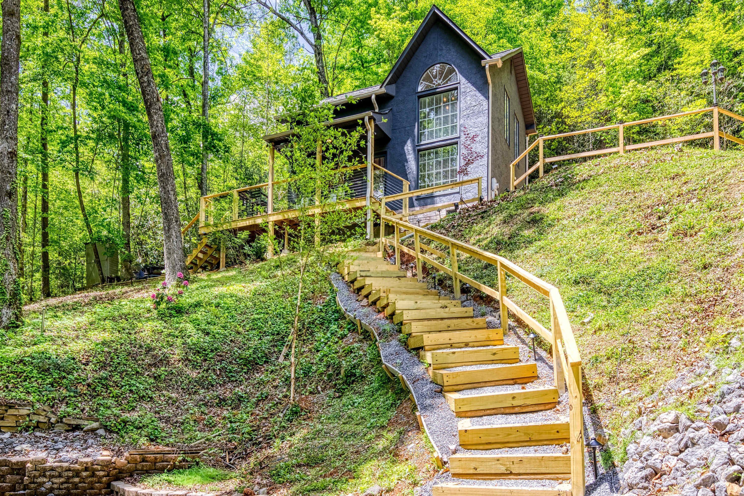 A wooden staircase leading to a blue building with a window, surrounded by trees.