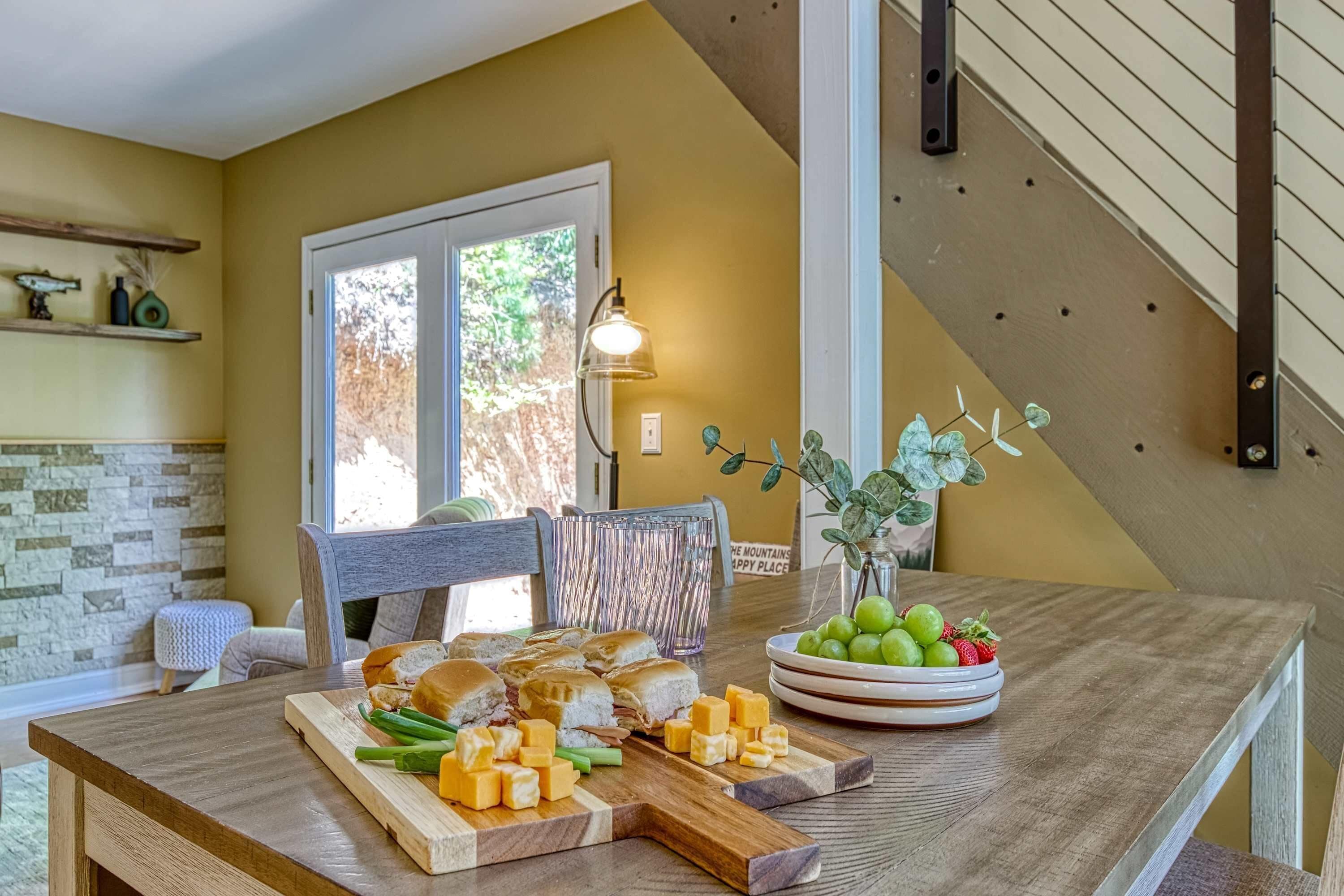 Un comedor con una mesa de madera, un cuenco de fruta y una ventana con vistas a árboles.