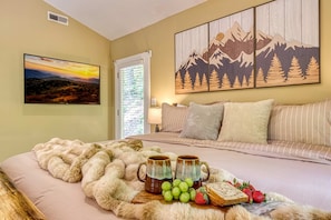 A bedroom with a bed, a painting of mountains, a window with blinds, and a tray with fruits and mugs. - Pine and Peak - Hot Tub Fire Pit Dog Friendly - Gatlinburg Arts Crafts Community - Sleeps 6 (Gatlinburg)