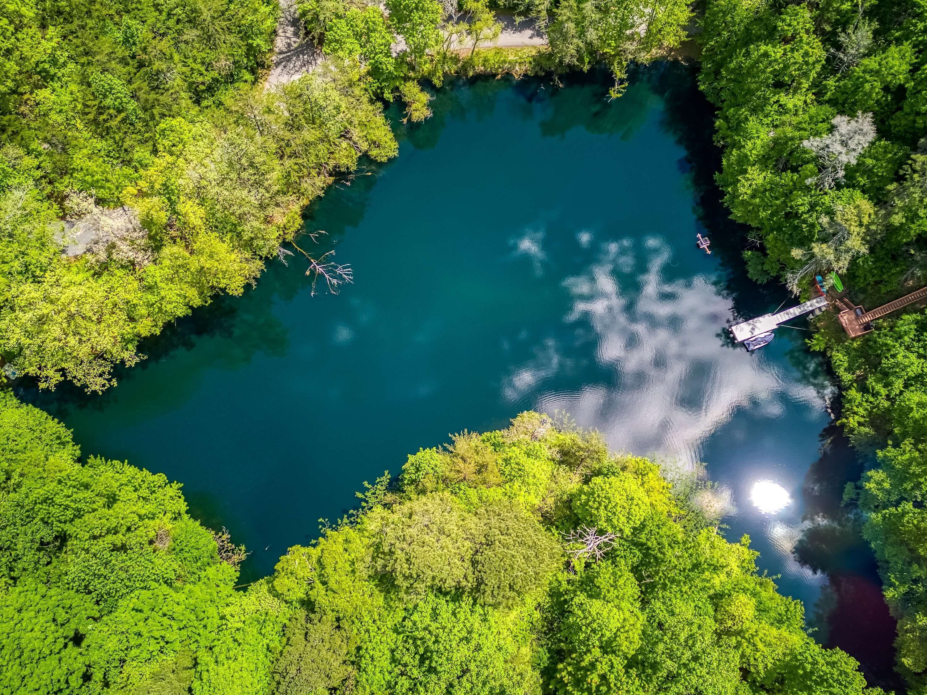 An aerial view of a serene lake surrounded by dense greenery, with a small dock extending into the water.