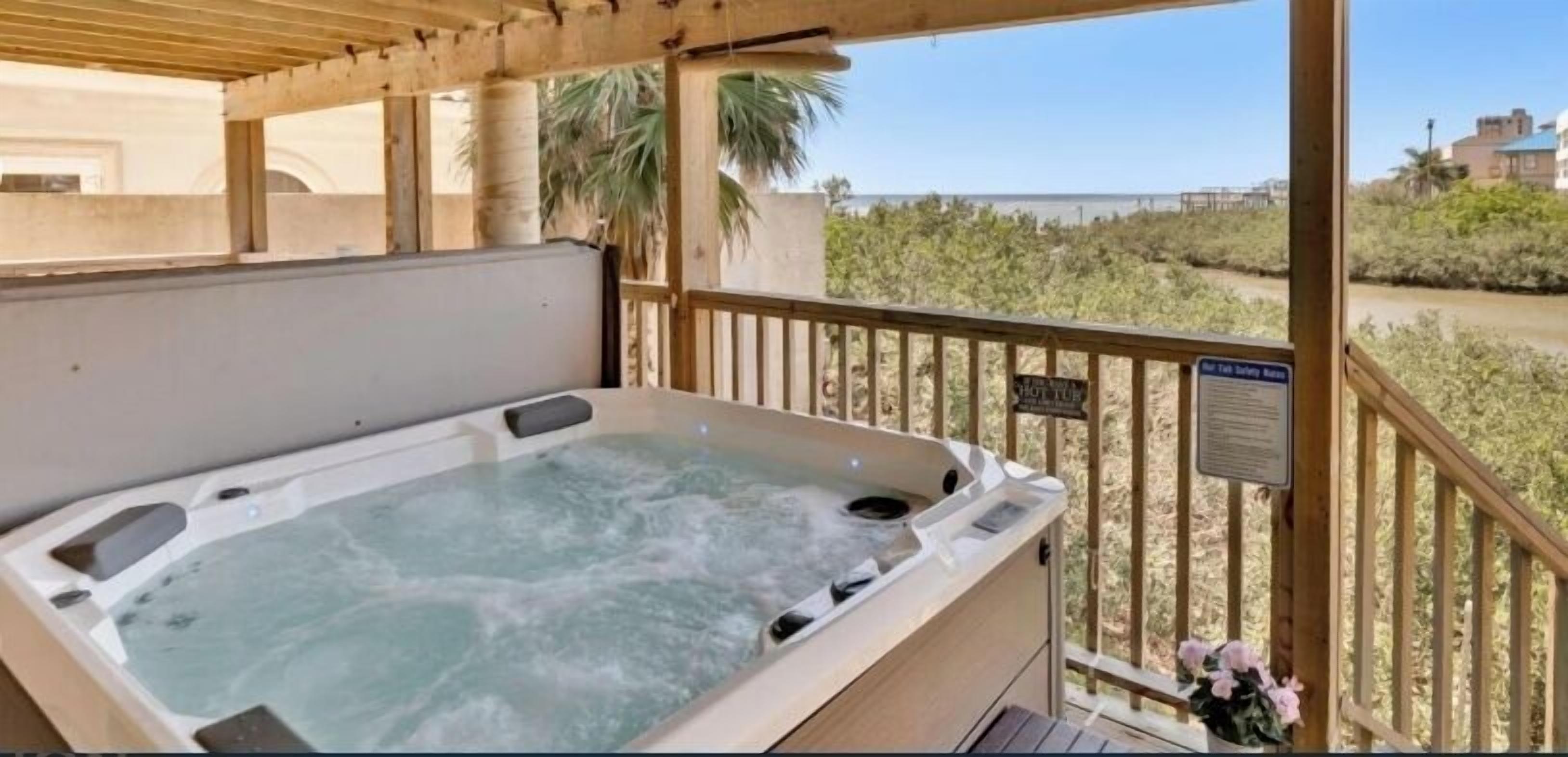 A hot tub on a balcony with a view of the beach and a sign indicating a safety rule.
