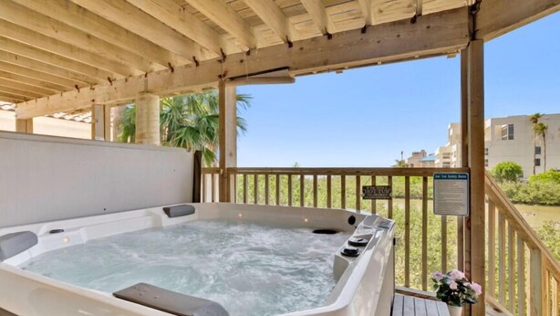 Un jacuzzi bajo una pérgola de madera con vistas a palmeras y un cartel que indica una zona de seguridad.