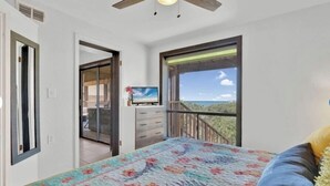 Un dormitorio con cama, televisor, ventana con vistas y ventilador de techo.