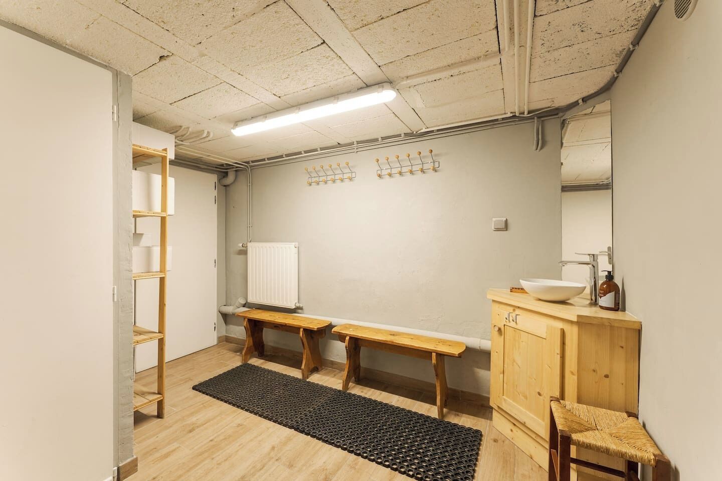 Une salle de bain avec un banc en bois, un lavabo, un miroir et un radiateur.