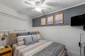 Una camera da letto con un letto, una ventola a soffitto, una televisione e opere d'arte appese al muro.