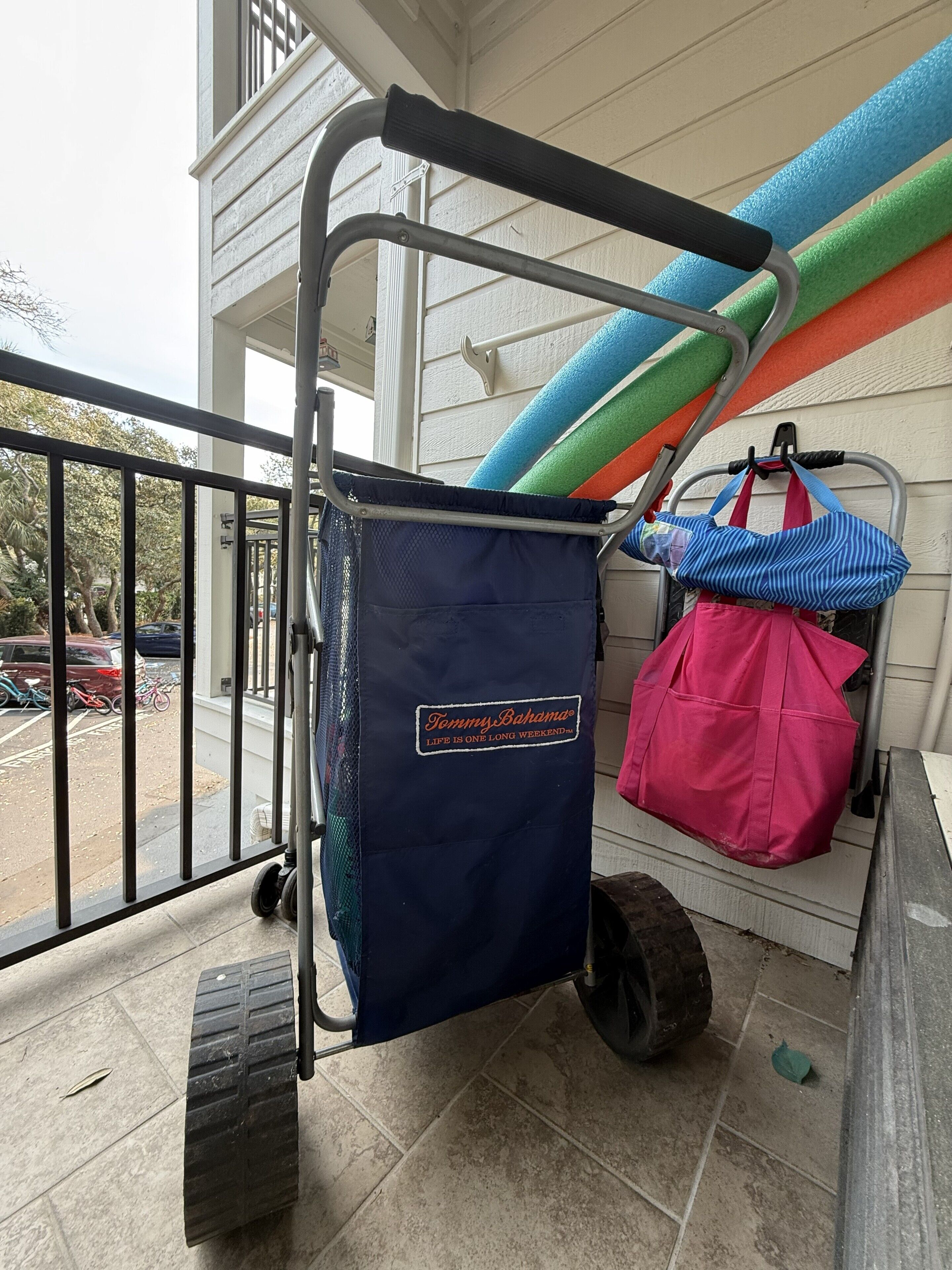 Un carrito de equipaje con una bolsa azul que dice 'TommyBahama Life is One Long Weekend' y una bolsa rosa en un balcón.