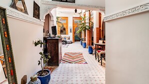 A hallway with a patterned rug, potted plants, and a large mirror on the wall.