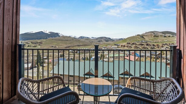 A balcony with wicker chairs and a small table, overlooking a valley with mountains and a body of water. - Vista Rubino. Bright Timberline condo with lift access, views, trails, and shuttle. (Mt Crested Butte)