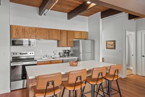 Een moderne keuken met houten kastjes, roestvrijstalen apparatuur, een centraal eiland met barkrukken en een houten plafond.