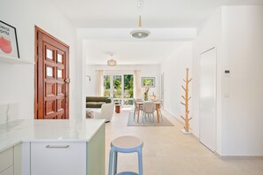 A modern kitchen with white cabinetry, a dining area with a table and chairs, and a view of the outdoors through large windows. - Villa Rosa Lia, swimming pool, pétanque, near the sea (Carqueiranne)