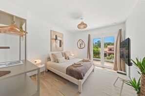 A modern bedroom with a bed, bedside table, lamp, TV, and a view of the outdoors. - Villa Rosa Lia, swimming pool, pétanque, near the sea (Carqueiranne)