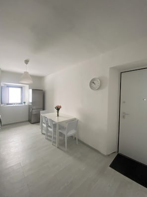 A modern kitchen with white cabinets, a refrigerator, and a dining area with a white table and chairs. - Coccodé, a perfect place for your detox (Cabatarcio)