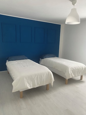 A bedroom with two beds, a blue accent wall, and a white ceiling light. - Coccodé, a perfect place for your detox (Cabatarcio)