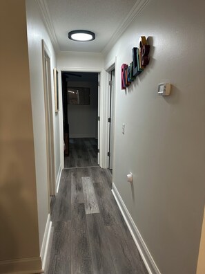 Un couloir doté d’un plancher en bois, de murs blancs et d’un luminaire au plafond.