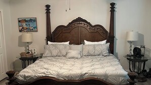 Ein Schlafzimmer mit einem Holzbett, einem Deckenventilator, einem Nachttisch mit Lampe und einem kleinen Tisch ebenfalls mit Lampe.