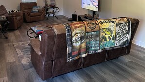 Ein Wohnzimmer mit einer braunen Ledersofa, einem Deckenventilator, einem Fernseher und einer Wand mit dem Schriftzug 'Happy Place'.