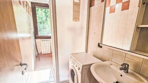 Ein kleines Badezimmer mit Waschmaschine, Waschbecken und Spiegel.