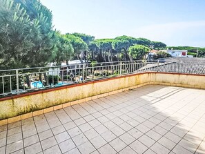 Eine Dachterrasse mit Fliesenböden, einem Metallgeländer und Blick auf Bäume und Gebäude im Hintergrund.