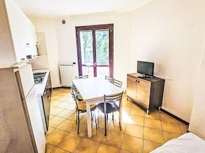 Eine kompakte Küche mit Esstisch, Stühlen, Kühlschrank, Herd, Heizkörper und einem Fernseher auf einem Schrank.
