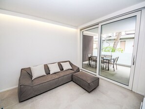 Ein modernes Wohnzimmer mit einer Eckcouch, einer Glastür, die zu einer Außenpatio führt, und Blick ins Freie.