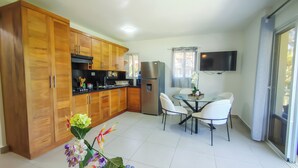 Una cocina moderna con armarios de madera, un refrigerador, una mesa de comedor con sillas y un televisor montado en la pared.