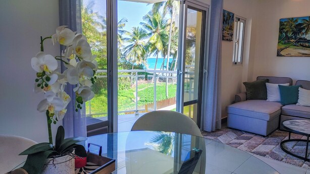 Una habitación con una mesa de vidrio, un sofá y vistas a palmeras y una playa.