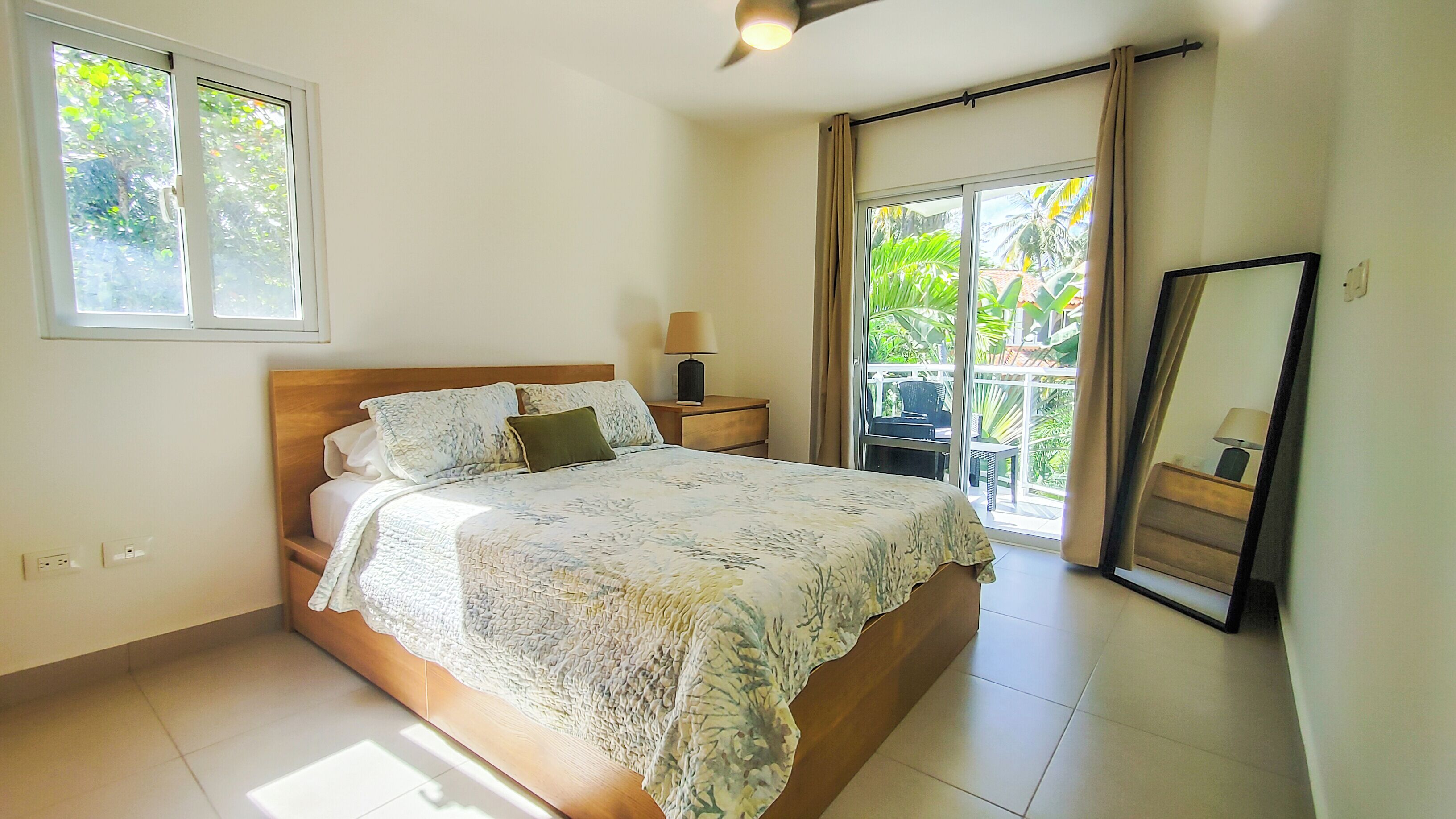 Une chambre à coucher comprenant un lit, une table de chevet, une lampe et une vue sur l’extérieur grâce à une porte coulissante.