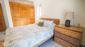 Un dormitorio con cama, mesita de noche, lámpara, armario de madera y ventana.
