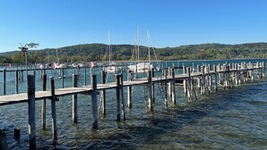 Eine Pier, die sich in ruhiges Wasser erstreckt, mit vertäuten Booten, umgeben von einem bewaldeten Hang.